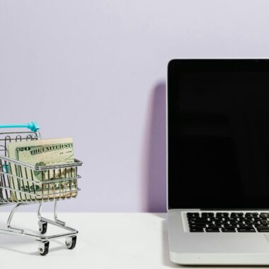 Shopping cart with money next to a laptop symbolizing online shopping and e-commerce.